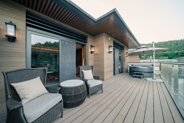 A modern outdoor deck with wicker furniture, a hot tub, and a glass balustrade overlooking a scenic view.