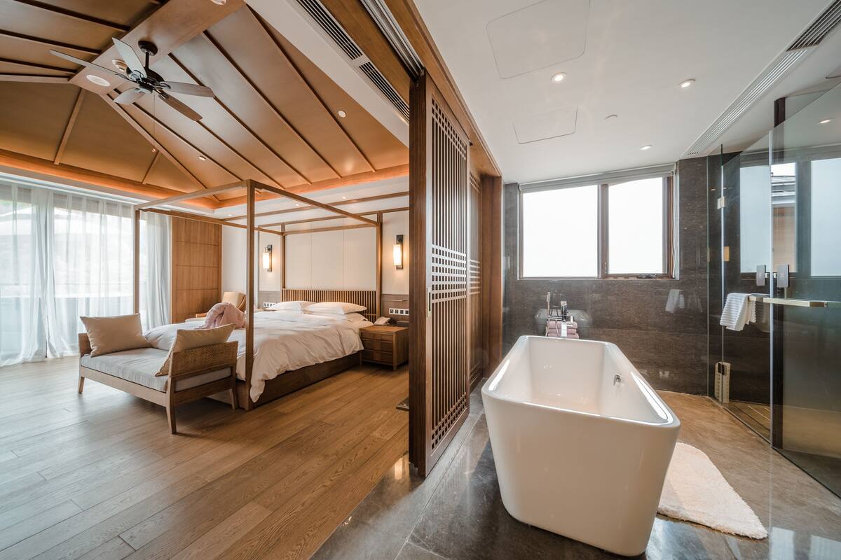 Una habitació d'hotel moderna amb un llit gran, una zona de seients separada, una banyera i una dutxa de vidre.