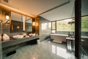A modern bathroom with a large mirror, three sinks, a bathtub, and a view of greenery outside.