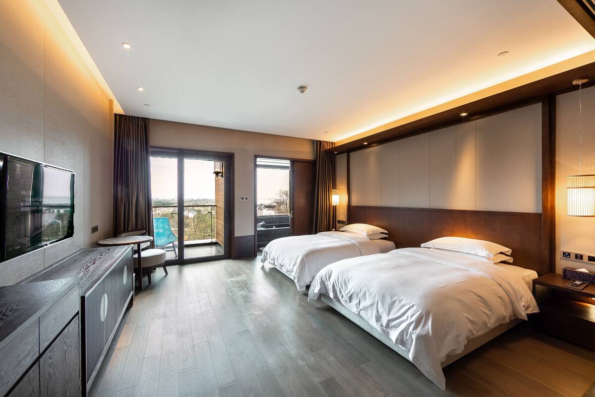 Una habitació d'hotel moderna amb dos llits, una televisió, un escriptori i un balcó amb vistes.