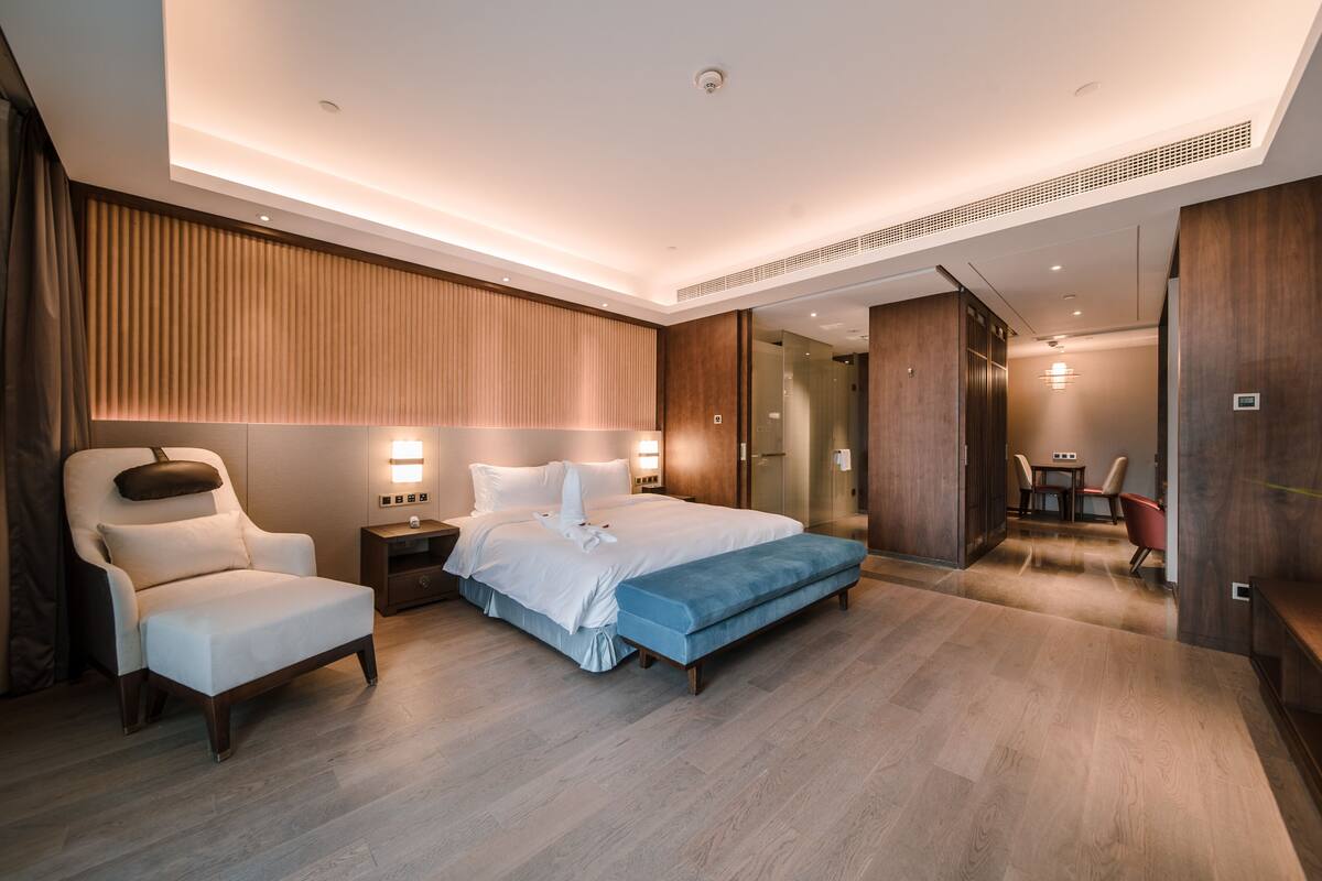 Habitació d'hotel moderna amb un llit gran, una zona de seients amb una banca i una petita taula amb cadires.
