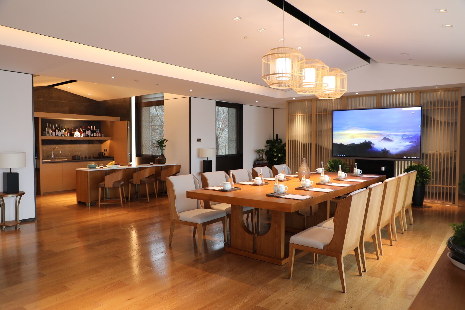 A modern dining area with a long wooden table, multiple chairs, and a large flat-screen TV on the wall.