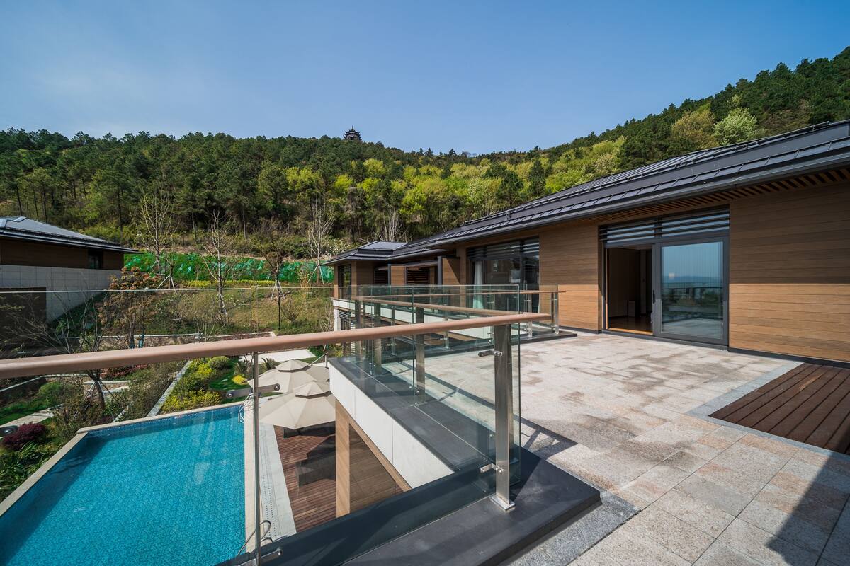 Un edifici modern amb un balcó de vidre que ofereix vistes a una piscina i vegetació exuberant.