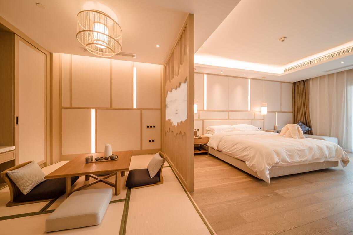 Habitació d'hotel moderna amb sòl de fusta, un llit amb roba de llit blanca, un escriptori amb cadira i una partició de tipus japonès tradicional.