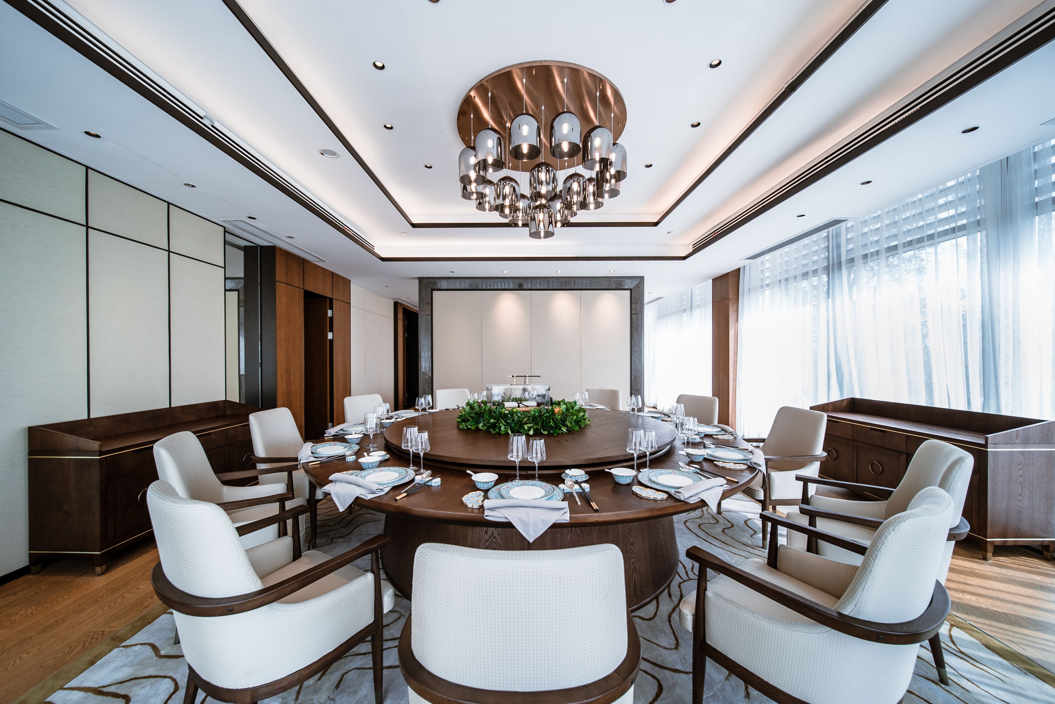 A modern conference room with a round table, white chairs, and a chandelier.