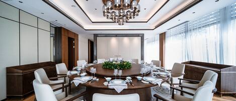 A modern conference room with a round table, white chairs, and a chandelier.