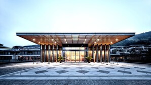 A modern building with a large entrance, a wooden slatted roof, and a paved area in front.