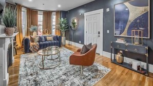 A modern living room with a dark wall, a large abstract painting, a sofa, a coffee table, and a fireplace.