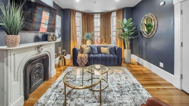 A modern living room with a dark blue wall, a fireplace, a large flat-screen TV, a blue sofa, and a round coffee table.