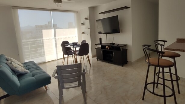 Una sala moderna con sofá, mesa de comedor, sillas, televisor y un balcón con vistas.