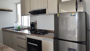Una cocina moderna con armarios de madera clara, un refrigerador de acero inoxidable, una cafetera y un lavavajillas.