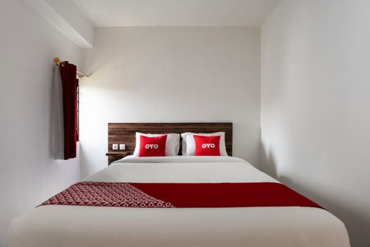 A hotel room with a bed, red and white bedding, and a wooden headboard.