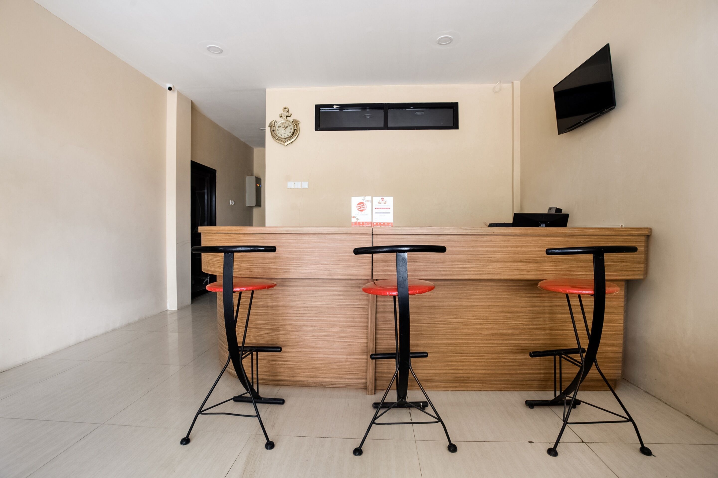 A reception area with a wooden counter, three red bar stools, a clock, and a flat-screen TV on the wall.