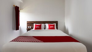 A hotel room with a neatly made bed, two pillows with the brand name "OYO," a red and white patterned throw, and a wooden headboard. - Capital O 3463 Cimahi Guest House (Cimahi)