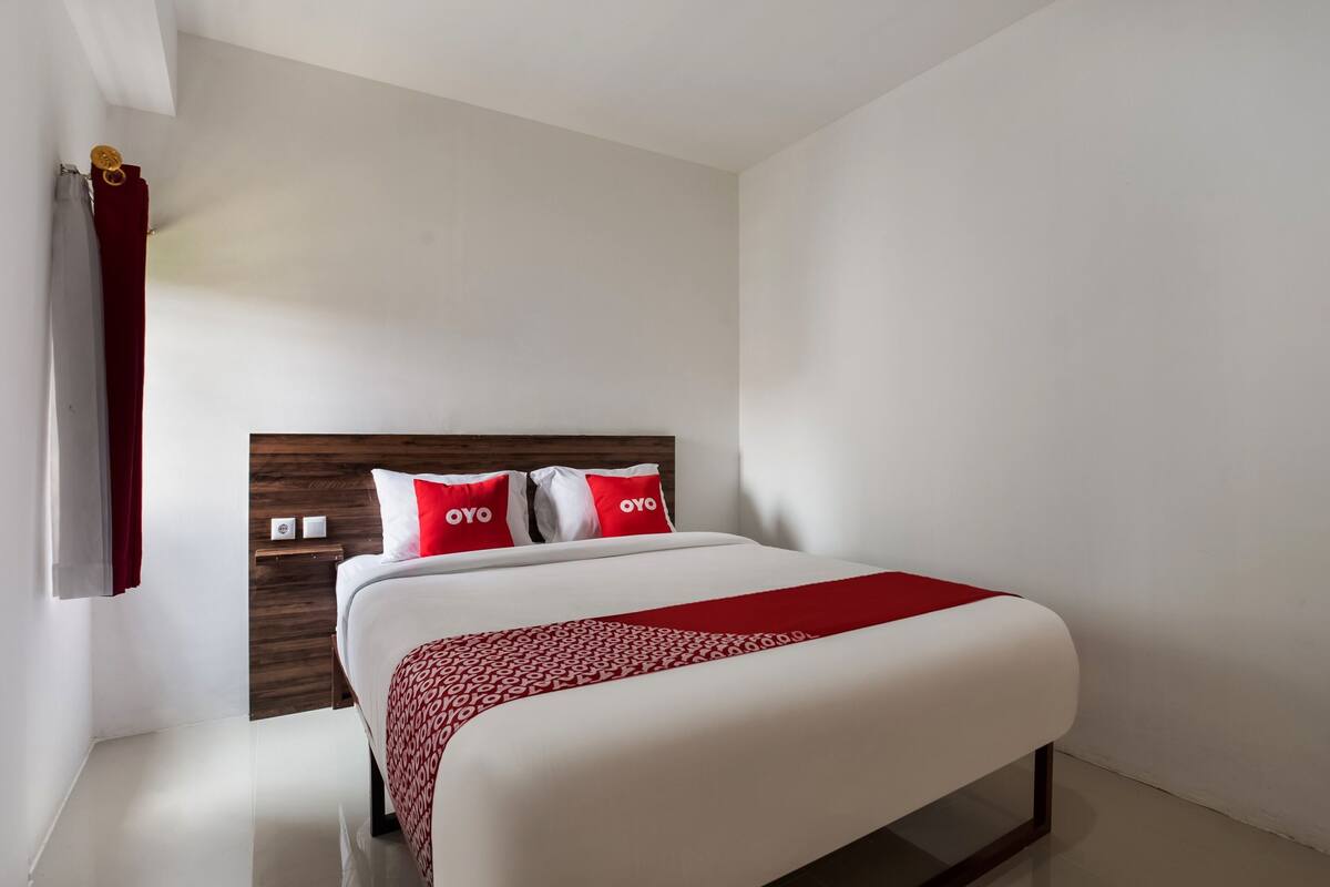 Habitació d'hotel moderna amb un llit gran, un panell de capçalera de fusta i una manta amb dibuixos vermells i blancs.