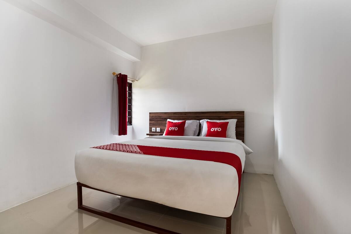 Habitació d'hotel moderna amb un llit gran, parets blanques i un panell de fusta al capçal.