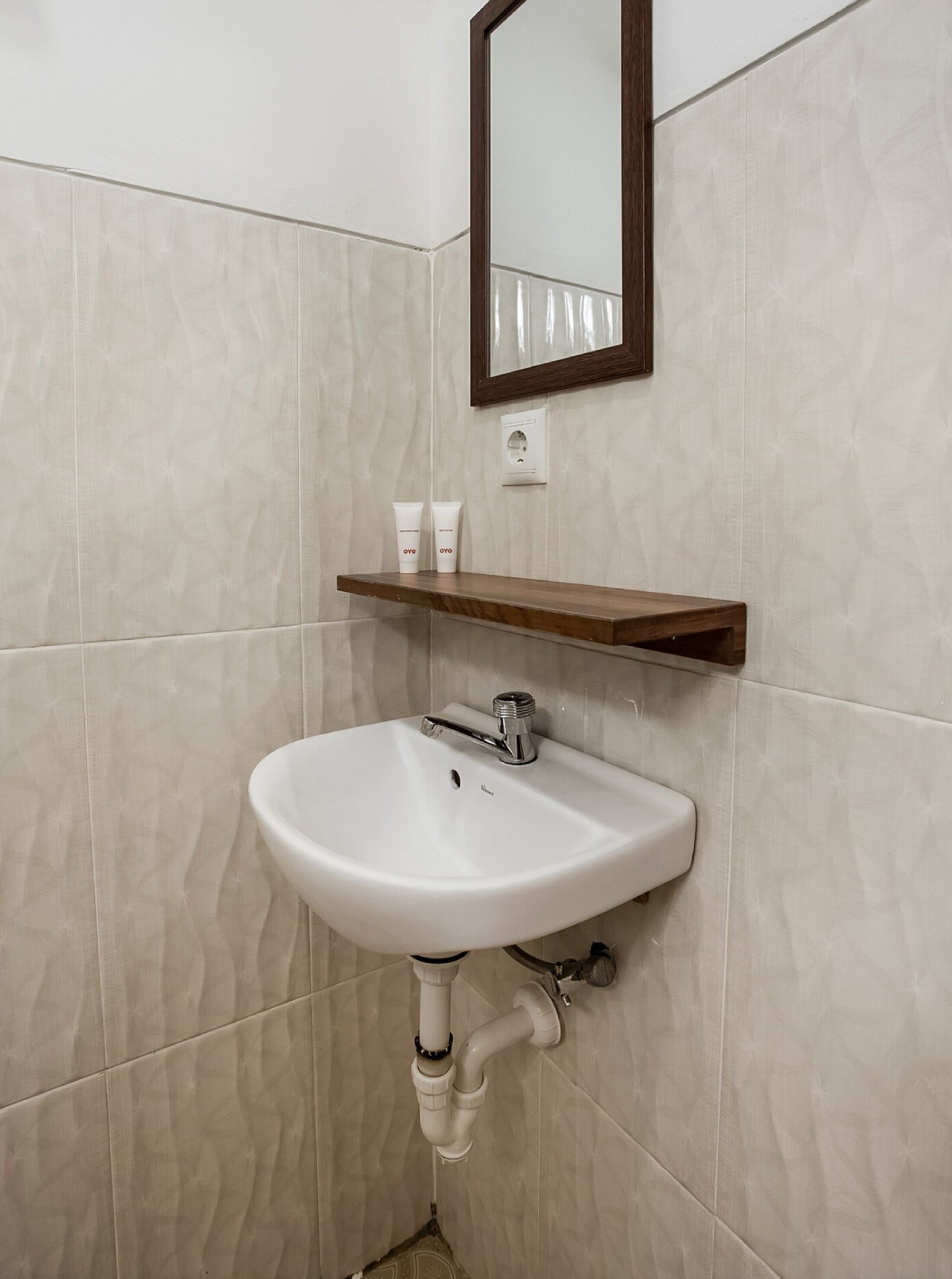 A bathroom with a white sink, a wooden shelf above it, and a mirror on the wall.
