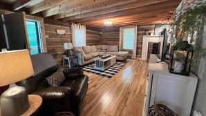 A cozy log cabin interior with a sofa, leather chairs, a coffee table, and a fireplace.