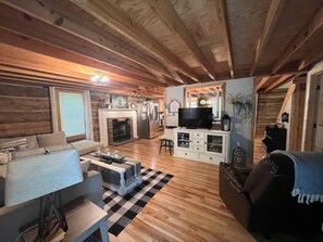 A cozy living room with wooden floors, a fireplace, a television, and a sofa. - Rustic Log Cabin near Wolf Creek Marina at Lake Cumberland! Perfect Getaway!  (Nancy)