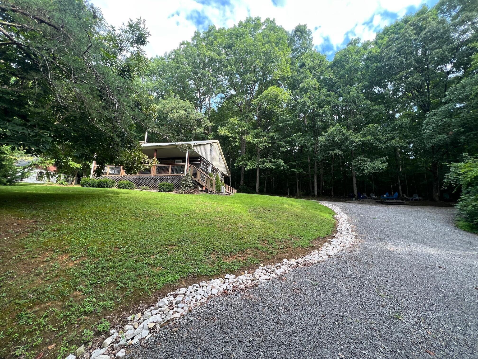 A house with a sloped roof and a porch, surrounded by a well-maintained lawn and dense trees.