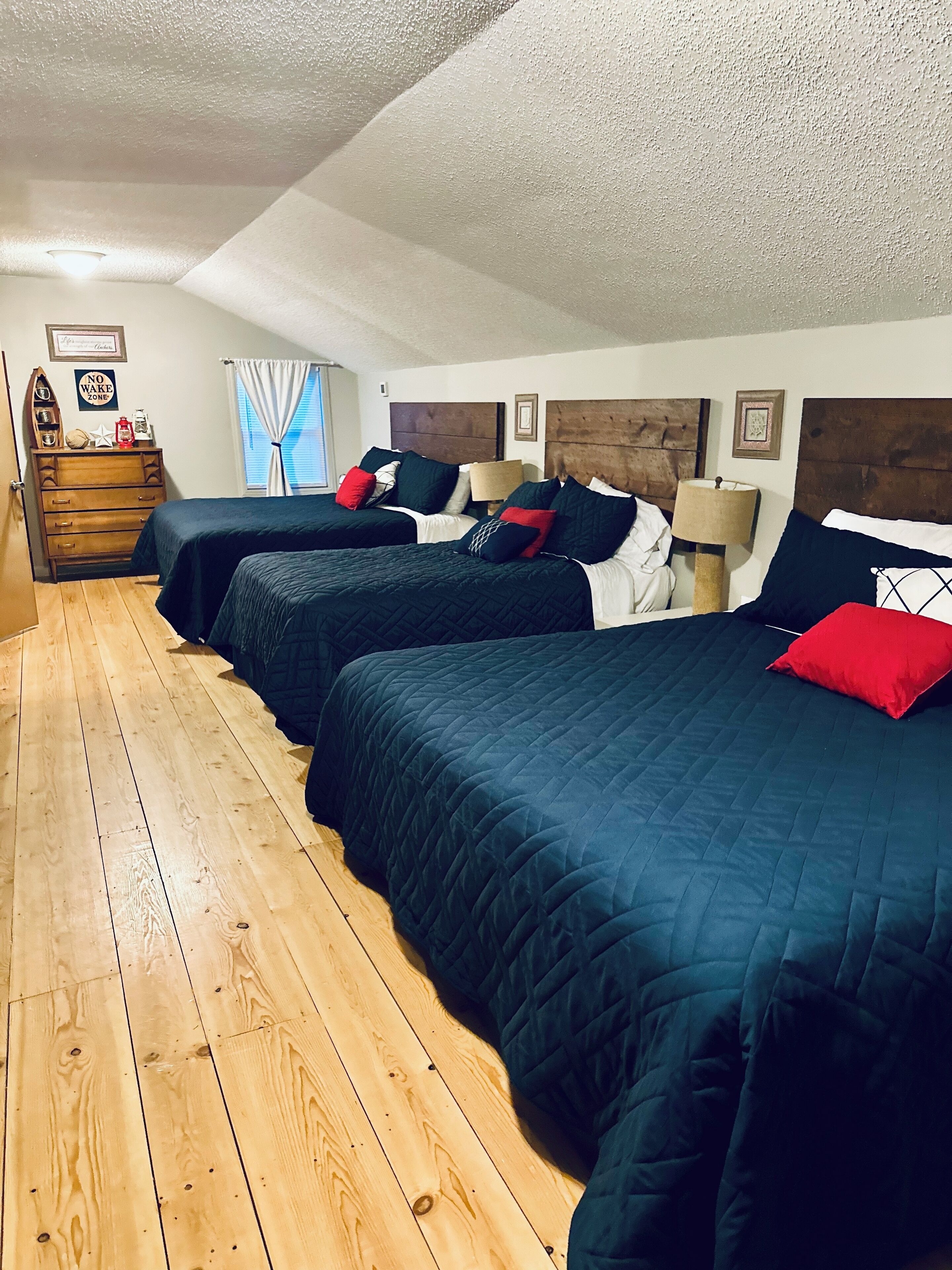 Un dormitorio con tres camas, suelo de madera y un aparador.