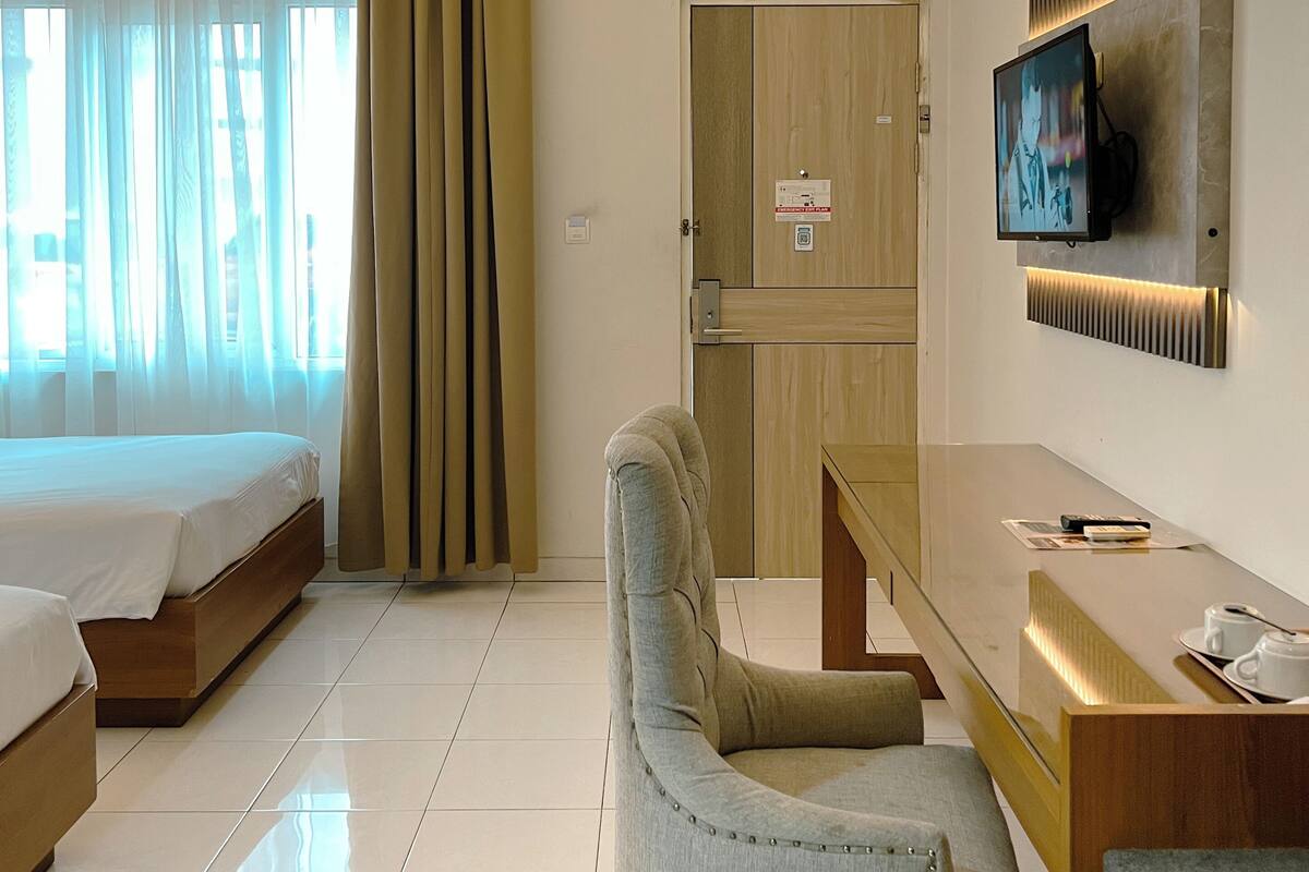 A hotel room with a bed, a desk, a chair, a television, and an air conditioning unit.