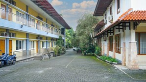 A courtyard with a paved walkway, a motorcycle, and a car parked in the distance. - Front One Resort Indraloka Temanggung (Temanggung)