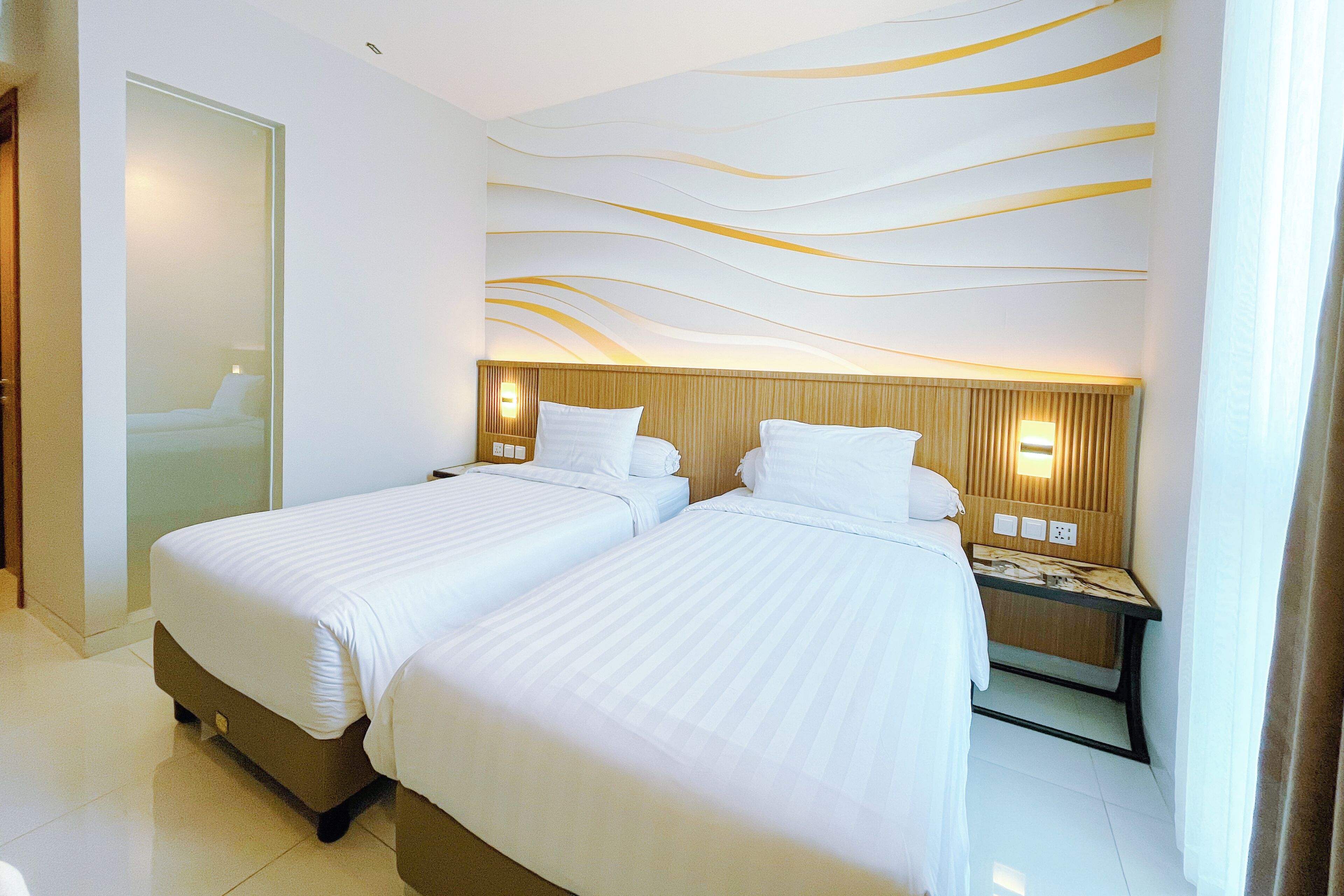 A hotel room with two beds, a wooden headboard, a nightstand, and a wall with a wavy pattern.