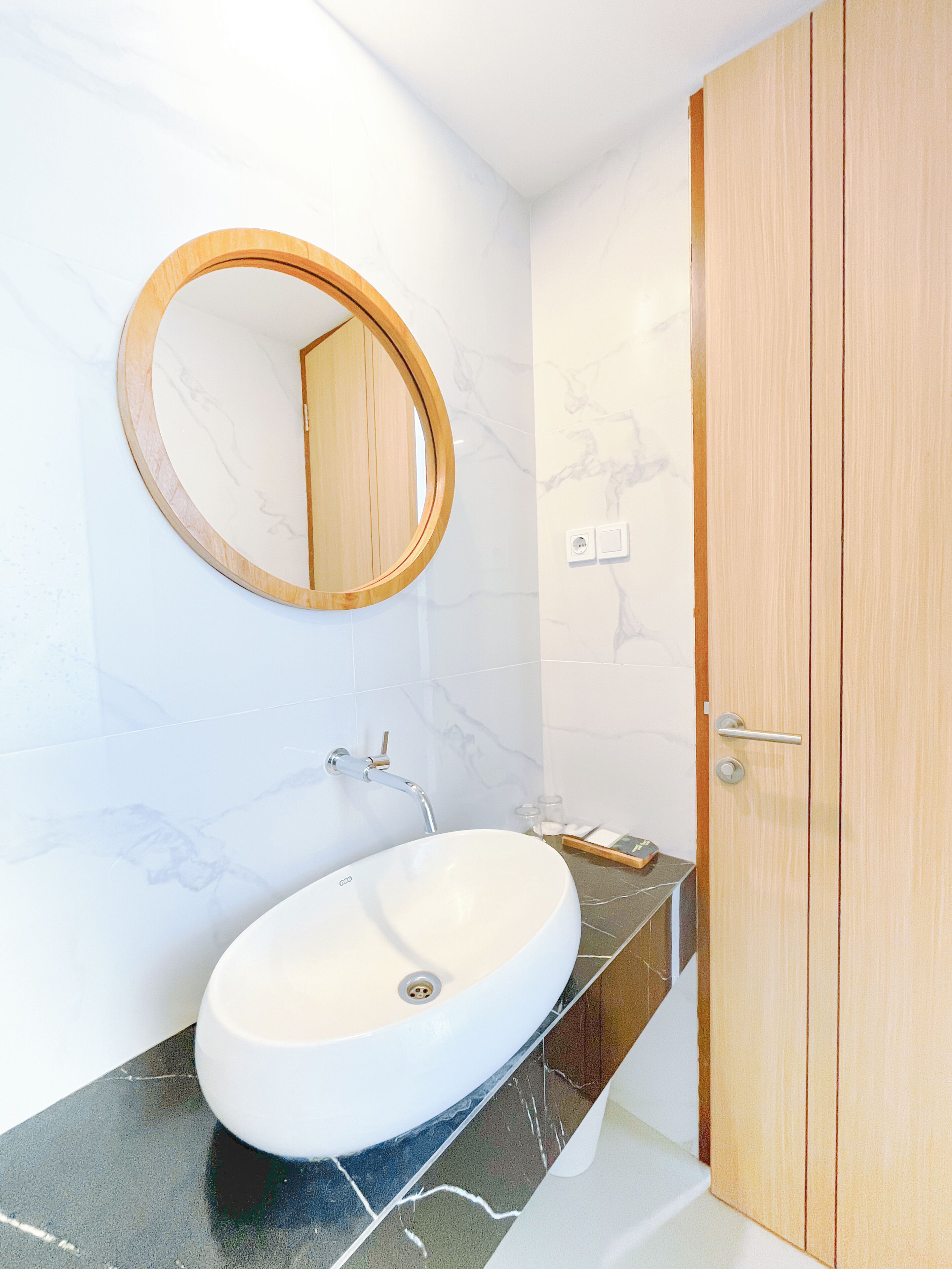 A bathroom with a round mirror, a white sink, and a wooden door.
