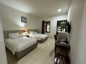 Two single beds with white linens, a table, and a wall-mounted TV.
