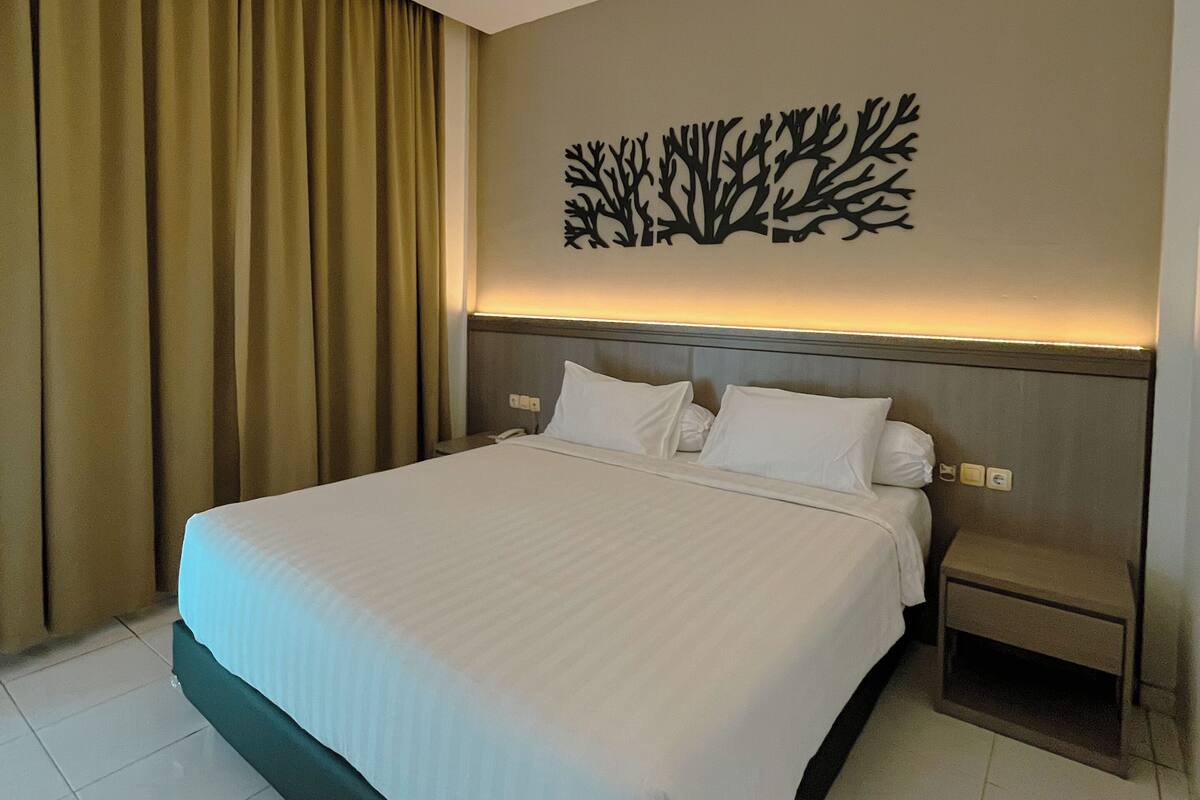 A modern hotel room with a large bed, a nightstand, and a wall-mounted artwork.