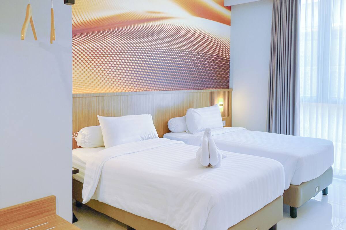A hotel room with two beds, a large window with sheer curtains, and a wall with a textured pattern.