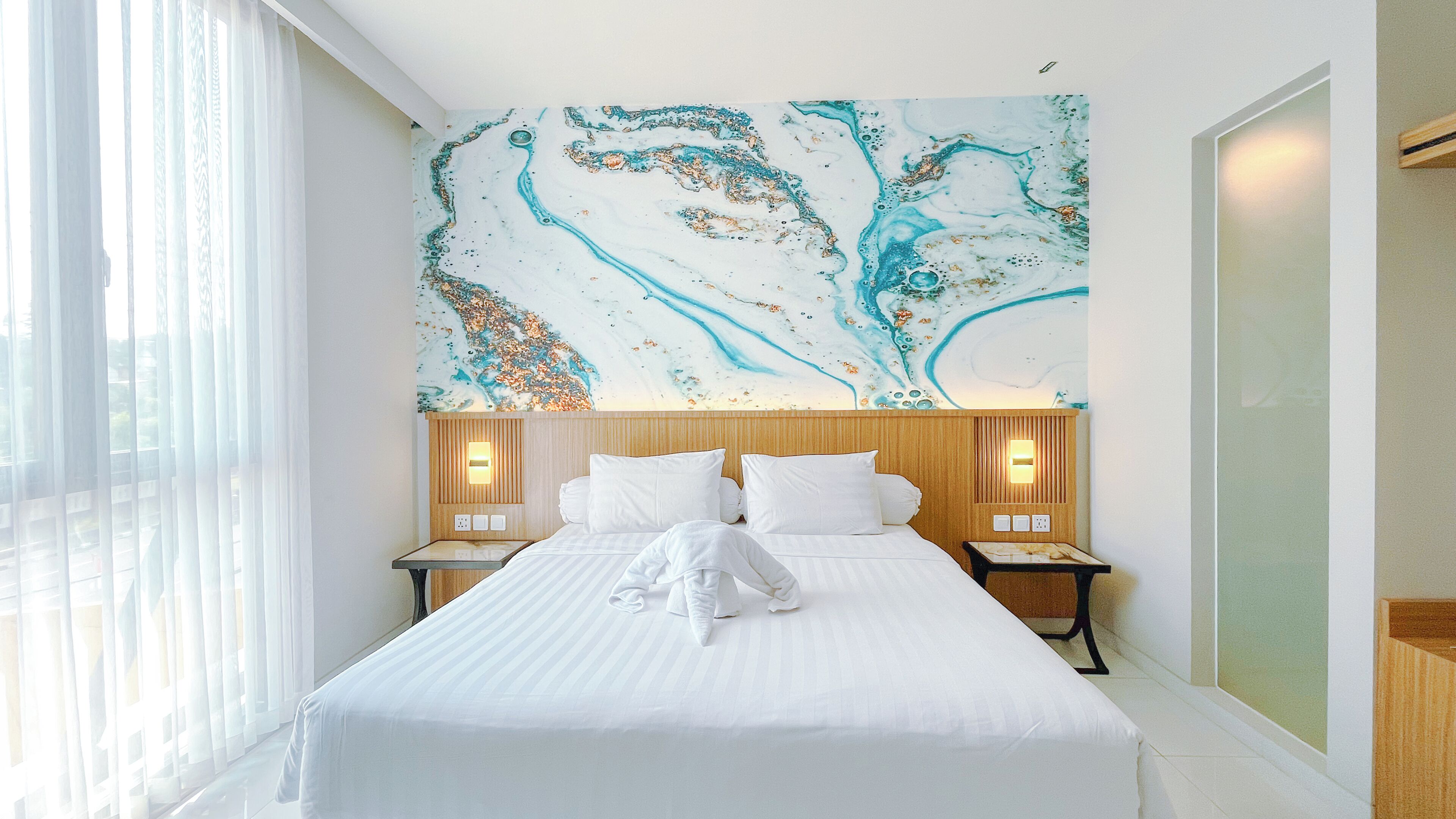A hotel room with a large bed, two bedside tables with lamps, a wooden headboard, and a large abstract painting on the wall.