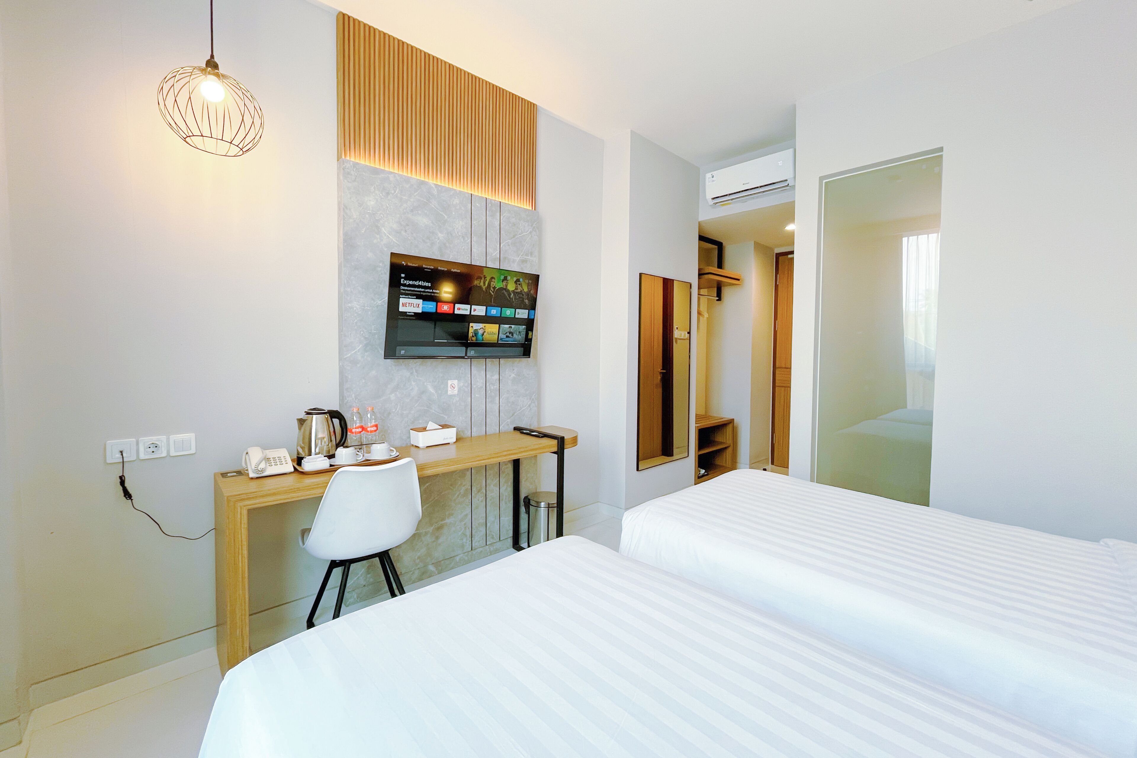 Quarto de hotel moderno com cama, escrivaninha com computador, cadeira, televisão na parede e espelho.