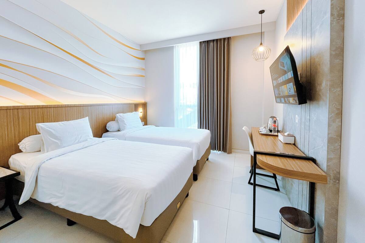 A hotel room with two beds, a desk, a TV, and a window with curtains.