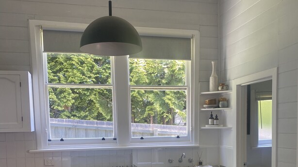 A kitchen with a central island, two bar stools, a hanging light fixture, and a window with a view of trees. - Yarra Cottage (Yarra Junction)