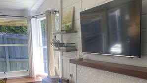A living room with a fireplace, a mounted TV, and a window with curtains. - Yarra Cottage (Yarra Junction)