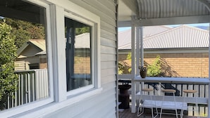 A covered outdoor area with a wooden bench, a table with chairs, and a view of neighboring houses. - Yarra Cottage (Yarra Junction)