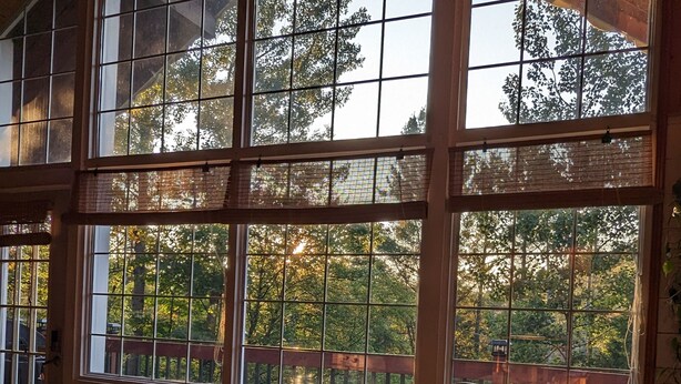 A dining area with a large window overlooking a wooden deck and trees. The table is set for four with plates, glasses, and a centerpiece. - Cozy cottage with hot tub! (Saint-Adolphe-d'Howard)
