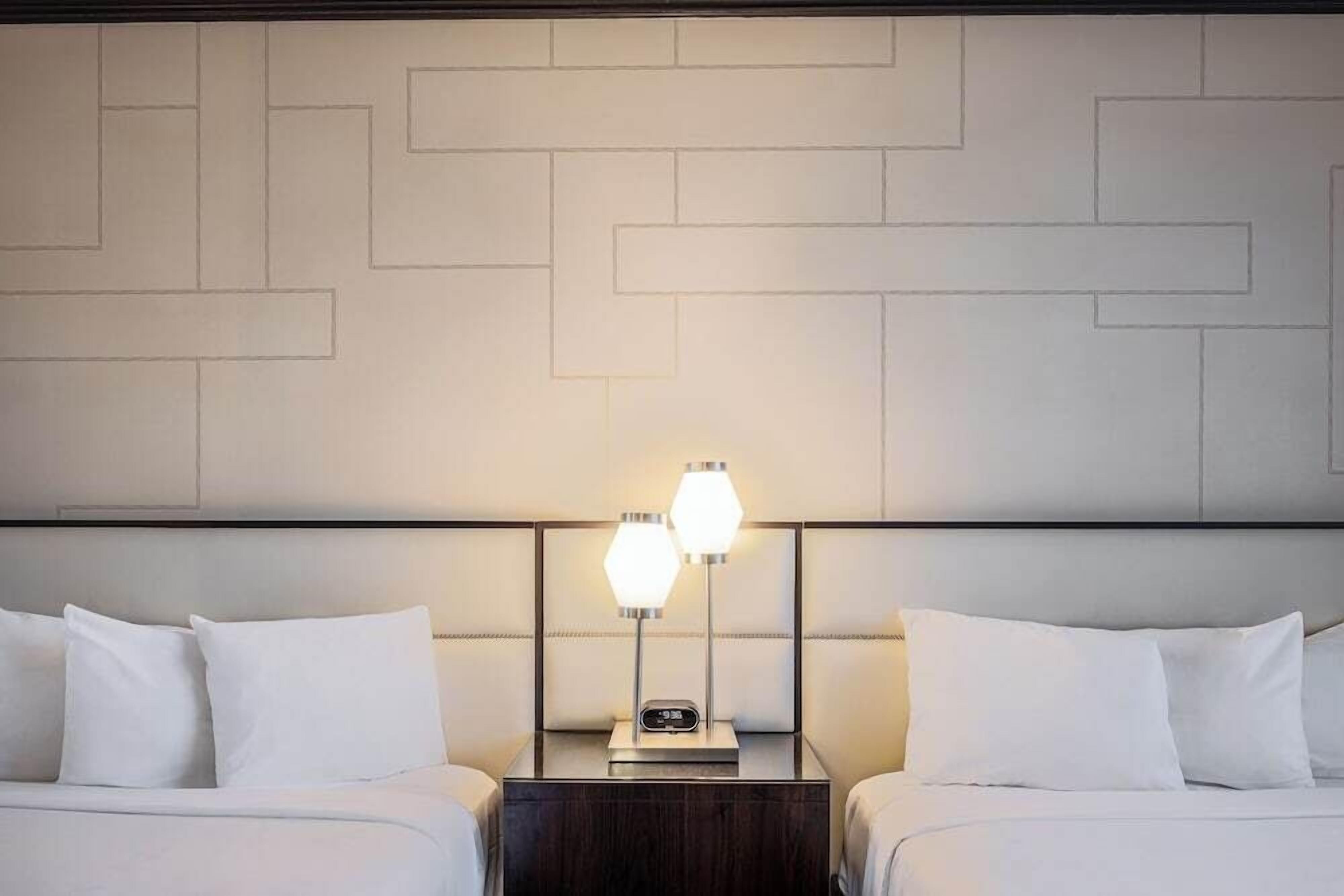 Une chambre d’hôtel avec deux lits, une table de chevet avec une lampe et un mur orné d’un motif géométrique.