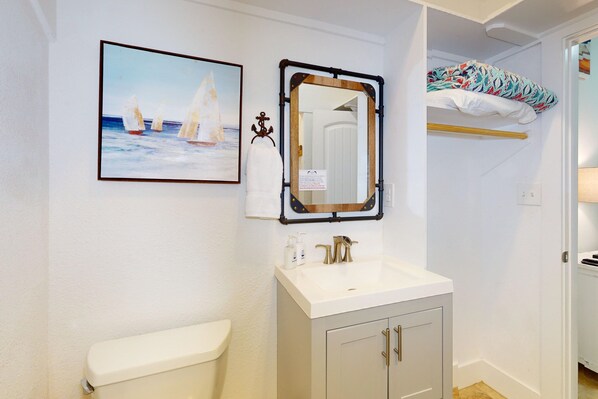 Une salle de bain avec un lavabo blanc, un miroir et un tableau encadré représentant des voiliers.