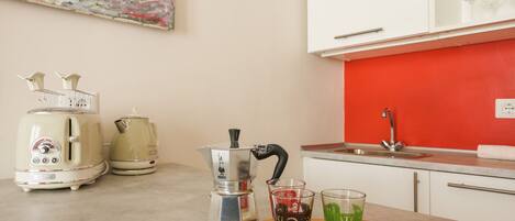 A kitchen with a red backsplash, a coffee maker, a kettle, and a toaster. There are two glasses on a wooden board.