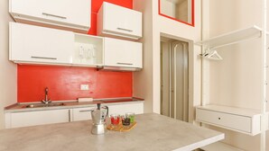Une cuisine avec des meubles blancs, un plan de travail rouge, un évier et un comptoir sur lequel se trouvent une machine à café et des verres.