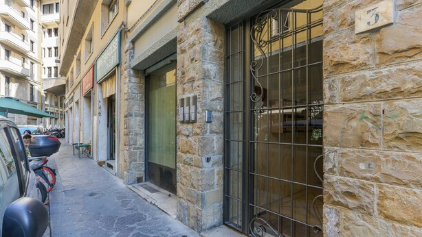 Une rue étroite bordée d’immeubles en pierre, avec une grille en métal et des scooters garés.