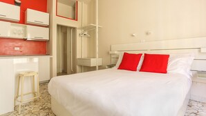 Une chambre d’hôtel avec un lit, un petit tabouret, une armoire et un miroir.