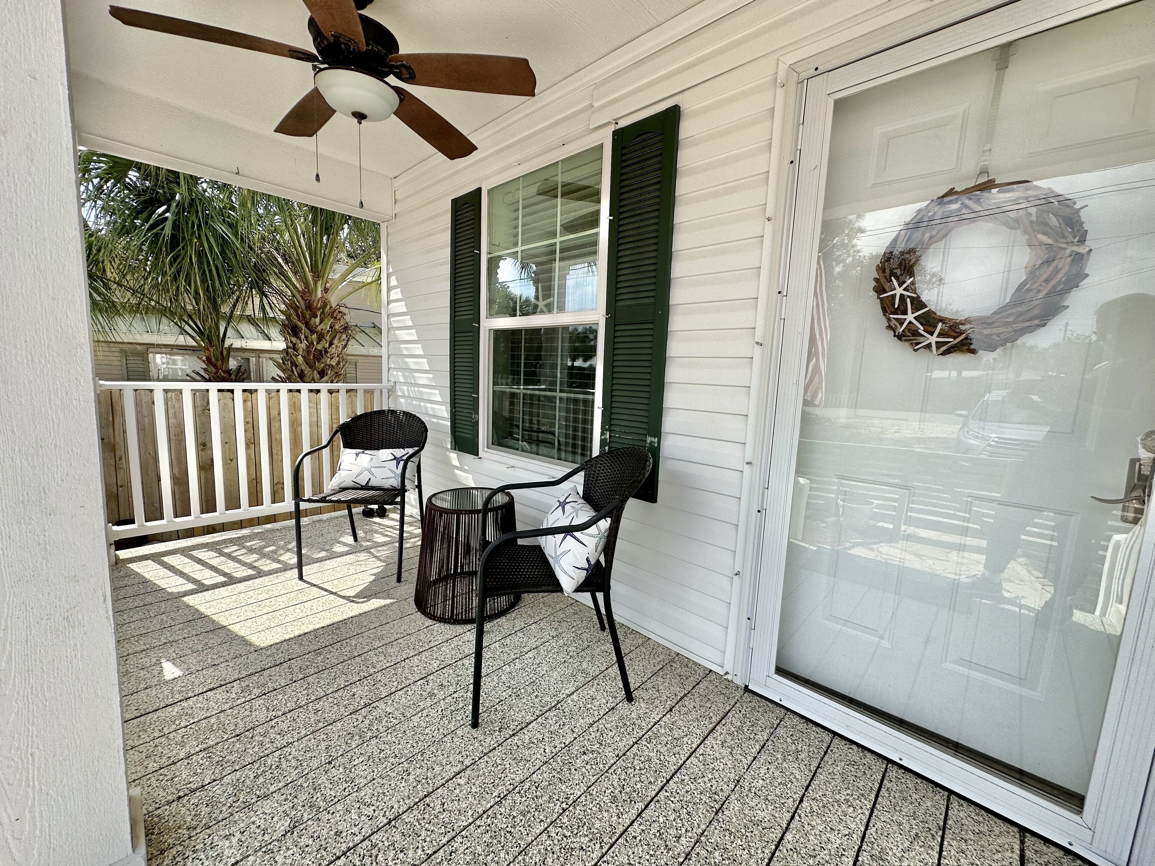 A covered porch with two chairs and a small table, a ceiling fan, and a decorative wreath on the door.