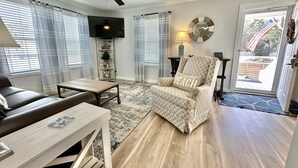 A living room with a ceiling fan, a TV, a sofa, a coffee table, a patterned armchair, and a rug.