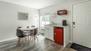 Eine kleine Küche mit einem weißen Kühlschrank, einer Mikrowelle und einer Kaffeemaschine. Es gibt eine Essecke mit einem runden Tisch und Stühlen.