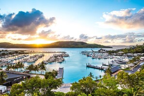 A marina with numerous boats docked, surrounded by lush greenery and hills in the background.