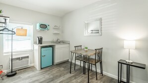 Una cocina compacta con un refrigerador azul, un microondas y un lavamanos. Hay una mesa de comedor con sillas y una lámpara de mesa pequeña.